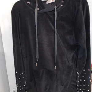 Hoodie - En svart hoodie från Madlady med vita pärlor på ärmarna och luvan. Hoodien är i satin material. 