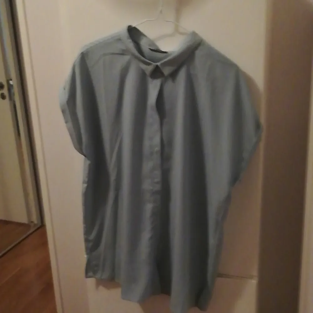 Lös, boxig blusskjorta med vikta korta ärmar och dolda knappar från Kiomi strl 42. Färgen är svår att beskriva, men närmast är nog mycket ljus grön/grå. Endast använd en gång, passar inte mig längre. Du står själv för fraktkostnad. . Blusar.