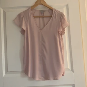Kortärmad blus från H&M  - Kortärmad v-ringad blus med lite puffiga armar från H&M i en rosa/beige färg.  Använd bara ett fåtal gånger, den har supersnyggt fall. I storlek 34, säljer för 60kr. 