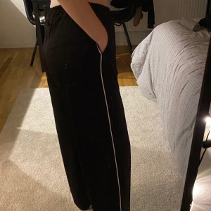 svarta tracksuitbyxor - sköna byxor, med vita linjer längdt sidorna och en söm mitt på framtill (se sista bilden) snörning i midjan. Drsgkedja nertill så att man kan knäppanupp och få slits på sidorna nedtill. Mjuka och sköna!