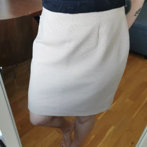 Mönstrad kjol - Beige/vit mini-hundtandsmönstrad kjol i strl C44, uppskattningsvis M/L. Måtten är midja 42 cm, höft 55 cm, längd 53 cm. Dragkedja bak. Köparen står för porto 55 kr. 