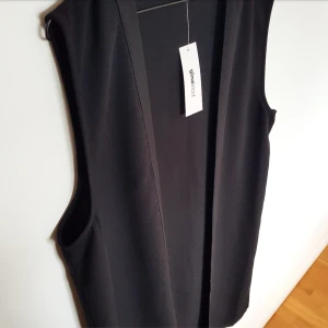 Lång svart väst från GinaTricot  - Lång svart väst från GinaTricot i strl XL(Men skulle säga en L). Köpt 2015 men aldrig använd och lappen sitter kvar. Köpt för 150 kr och säljs för 200 kr. Kan mötas upp i Stockholm eller skicka men köparen betalar frakt!🌻