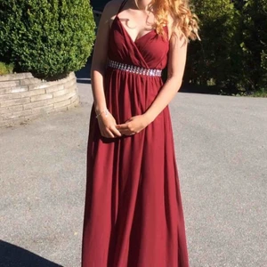  - Säljer min gamla balklänning den är använd en kväll. Den är mörkröd i storlek S men XS passar den även. Den har ett pärlband i midjan med massa pärlor som sitter på framsidan. Ryggen är öppen med ett enkelt kryss av banden. 