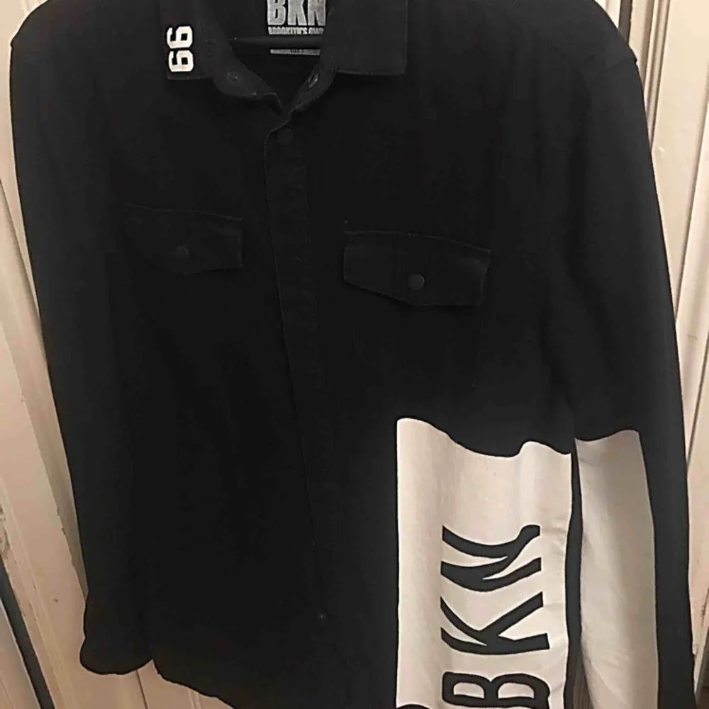 Svart jeansskjorta med vita detaljer i märket BKN Brooklyn’s Own by Rocawear. Storlek S men är stor i storleken. Funkar till både killar och tjejer. Endast använd 2 gånger - som ny!! . Skjortor.