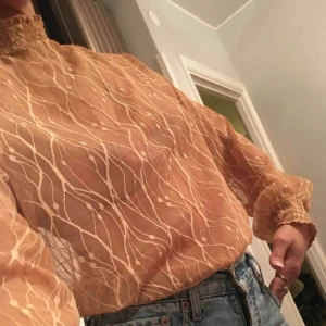  - Transparent nude blus i strl M passar L och S beroendes på hur man vill att  dens ska sitta. Den har knappar i halsen bak och smockad polo och ärmslut