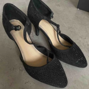 Fina skor med klack - Svarta, fina klackar med blänkande paljetter/stenar på. Använda ca 2 ggr så i väldigt fint skick.   Köparen står för frakt, 66kr. Skickas med postnord, spårbart.   