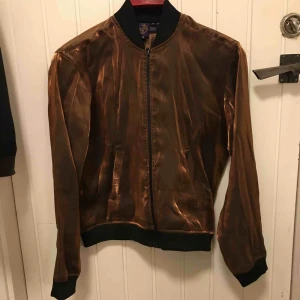  - Bomber jacka som är väldigt tunn. Använd 1 gång och är köpt på Beyond Retro. Skulle säga att den är mellan S/M i storleken. Skimrar fint i koppar. 