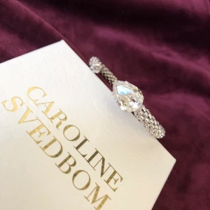 Caroline Svedbom armband Silver - Använt men fint, inget direkt att anmärka på. Den stora modellen  i silver med vit kristall. Nyp ca 995:- Säljer för halva priset!! 