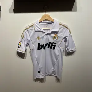 Säljer en replika av Adebayor Real Madrid tröja från säsongen 2011/12. Storlek: S. Tröjan har använts men är i mycket gott skick. Den klassiska vita designen med klubbens emblem och Adebayor's nummer 6 på ryggen gör den perfekt för samlare eller fans