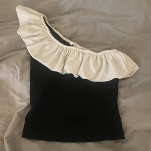 Svart topp  - Säljer denna svarta one shoulder toppen med vit volang från H&M 