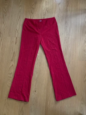Röda kostymbyxor med kritstrecksrand  - Fina röda bootcut, Lågmidjade kostymbyxor med vita ränder. I bra skick 