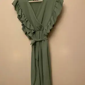 Ljusgrön klänning med volang från axlar och ner till midja. 
