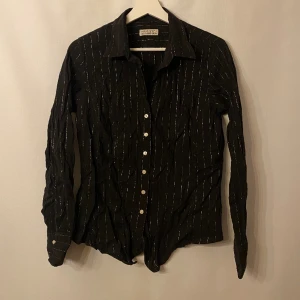 Svart/ guldrandig skjorta - Svart skjorta med guldiga ränder. Lite skrynklig på bilderna😅 Märke: The shirt factory. Storlek: L men de är snarare en XS/S. 