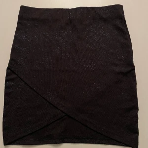 Svart kjol med blått glitter - Svart omlott kjol med blått glitter i tyget. Från Ginatricot, säljs pga passar ej längre 