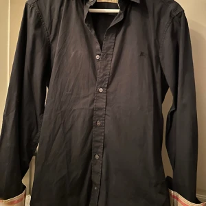 Burberry skjorta (svart) - Säljer en riktigt go burberry skjorta i storlek XS, materialet är lite tunnare. Gott skick. Tveka inte på att höra av dig om du har frågor.