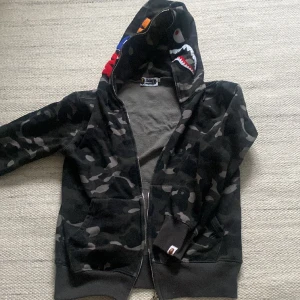 A Bathing Ape zip-hoodie - Väl omhändertagen Bape zip-hoodie. Tror inte den är äkta därav priset, men är i topp-kvalite. Storleken är M. Färgen är svart/grå.