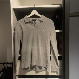 Långarmad Polo Ralph Lauren Piké - Grå Långarmad Polo Ralph Lauren Piké. Plagget är i använt fint skick. Storlek 14/16. Ny pris 950. Mitt pris 300.  OBS! Plagget är ganska liten i storleken.