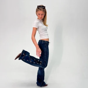 REMAKE LACED JEANS - Storlek: Midja (68cm), Innerbenslängd (79cm), total längd (102cm). Mörkblå, remake, lågmidjade, bootcut jeans med mörkblå slit och snörning på sidan och upptill. Modellen är 165 cm.