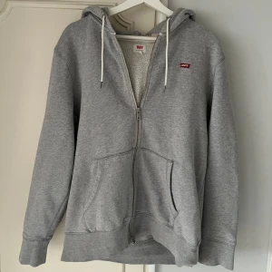 Hoodie - Ziphoodie från Levi’s i grå säljs. Storleken är i M och tröjan är i nyskick.