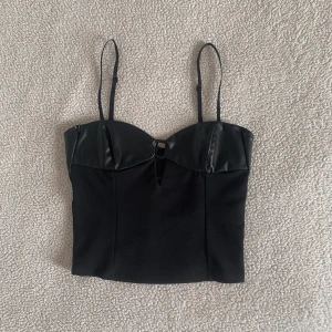 ZARA svart topp med PU-skinn - Supersnygg topp med PU skinn-detaljer från ZARA. Använd en gång. Har fått ett rivmärke under bysten, men inget som syns eller stör användningen av den. Dold dragkedja på ryggen.