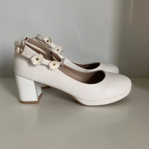 Vita klackskor - Vita klackskor i storlek 37 1/2 med söta små tusentjärnor på bandet som går runt vristen. Klacken är 6 cm hög. Använda och har några små repor och lite skavd vid sulan på höger skon. Innersulans längd är 24 cm🤍🌷