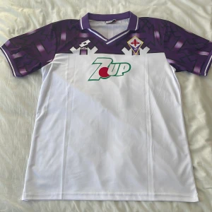 Snygg Fotbollströja till sommaren. - Säljer min helt oanvända ”Retro” Fiorentina fotbollströja. Med en fin design på tröjan och 7up loggan gör detta denna matchtröja ikonisk.  10/10 skick Har aldrig användit mig av tröjan då den är lite för stor för mig. 