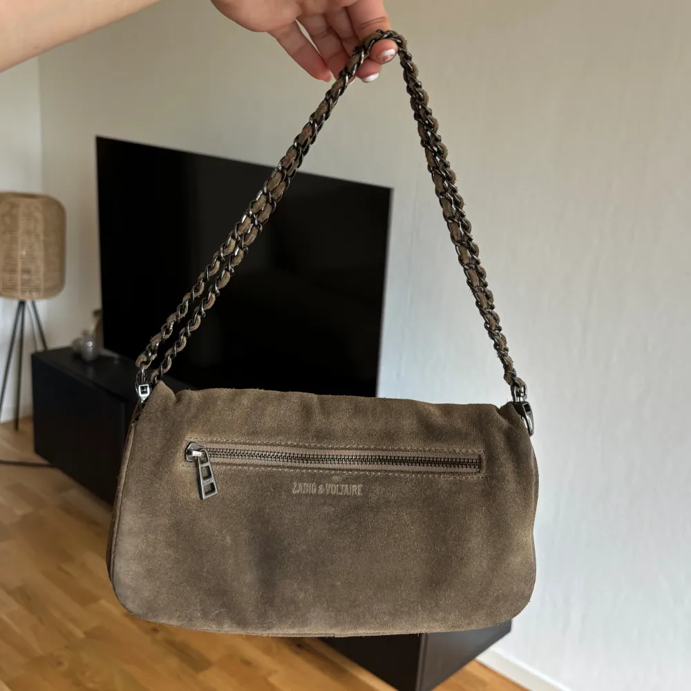 Väska från Zadig & Voltaire i brun/mörk beige mocka, modellen Rock. Bra begagnat skick! Både det långa och korta bandet medkommer. Givetvis äkta. . Laukut & Käsilaukut.