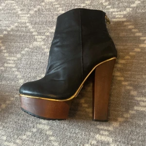 Högklackad stövlett - Ytterst lite använda stövletter från Tiamo. Köpta på Scorett. Har legat i förrådet, dessvärre fått några små skrapmärken på klacken och på skon.  Svart fejkskinn, Dragkedja på insidan. 14 cm hög klack, 4 cm klack fram. Nypris 2000kr. 