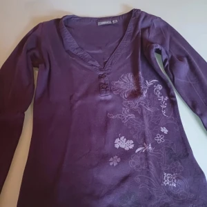 Tröja - Föremålsbeskrivning Långärmad blus i mycket fint skick. V-ringning med knappar. Mått: axlar 32, armhålor 40, midja 33, botten 37, längd 56 cm.