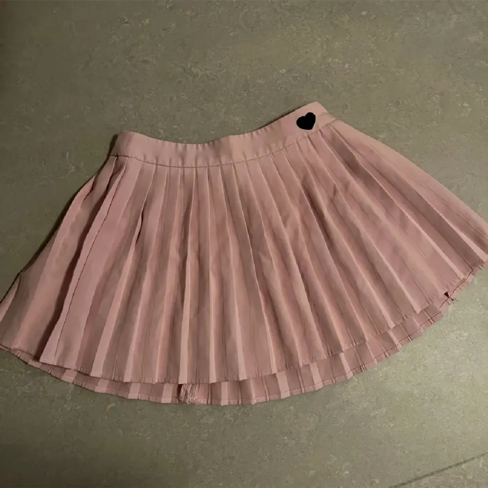 En rosa plisserad kjol med ett svart hjärta vid sidan av midjan, från Shein i strl 36!  OBS! Väldigt kort. Kjolar.