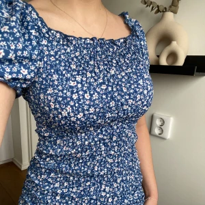 Blommig blå klänning - Så fin blommig klänning. Väldigt stretchiga material och luftig, så fin på sommaren! Aldrig använd. 