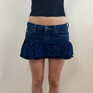 REMAKE LEOPARD KJOL MED VOLANG - midjemåttet är 36 cm tvärs över, längd fram är 25 cm, längd bak är 34 cm. Remake leopard minikjol med två volanger. Sydd av två olika original jeans. Modellen är 165 cm