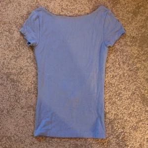 Blå öppenryggad T-shirt  - Blå tajt t-shirt med djup öppen rygg från Gina Tricot. Endast använd ett fåtal gånger så den är i väldigt bra skick! Säljer då jag inte använder den.  Måtten är från hals till nedersta kanten 47cm, 27cl bred och från ärm till ärm 42cm.