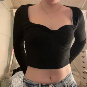 Långärmad tröja med detalj  - En långärmad lite kortare tröja med en snörr detalj mellan brösten.