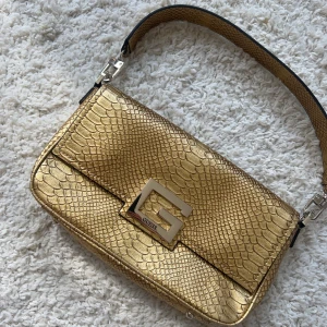 Guess handväska  - Helt ny och oanvänd Guldig handväska från guess, ett långt band medföljer. Köp sker via köp nu, jag postar inom 24 h 