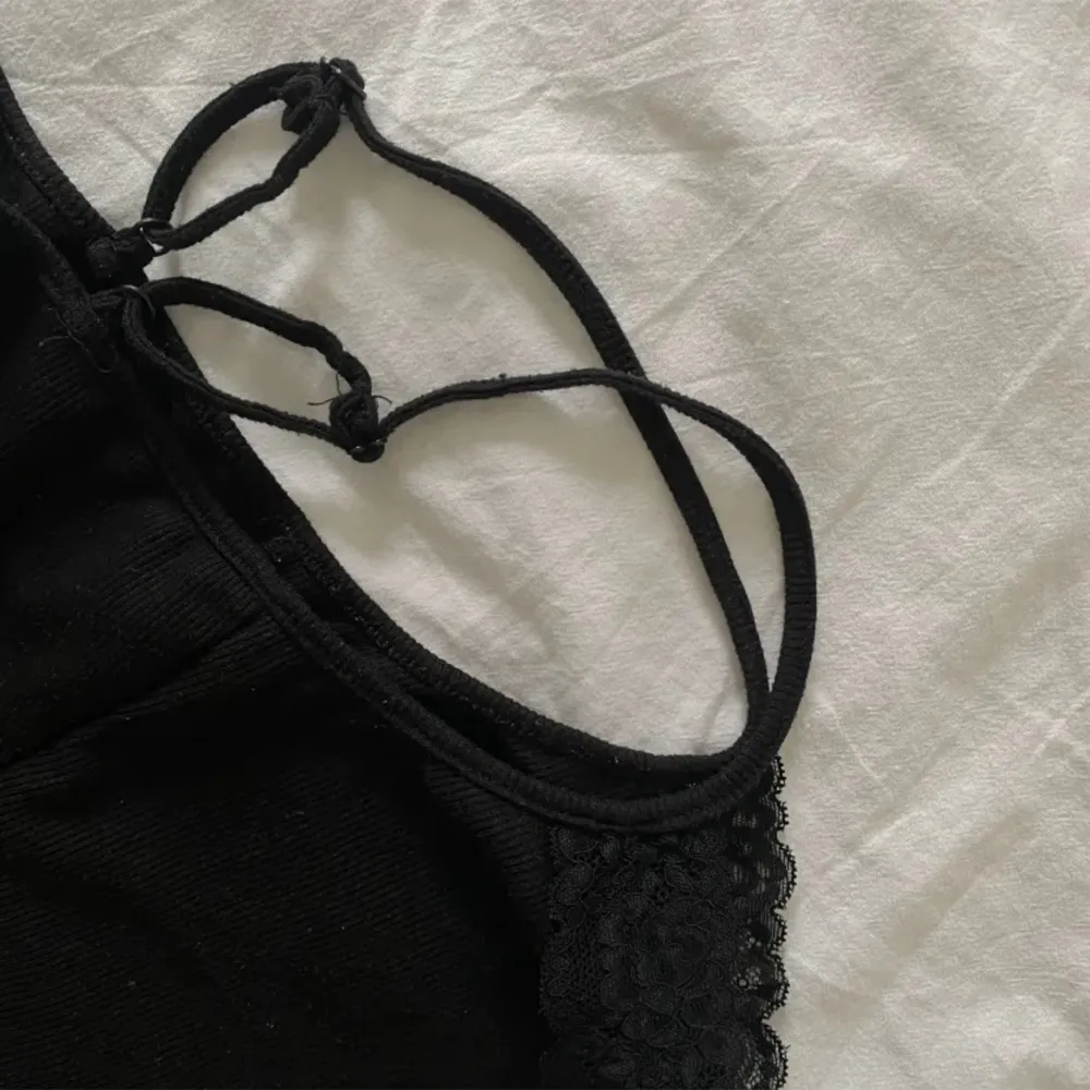 Ett svart ribbat linne med spetskant, superfint som det är, eller under en button up eller kofta. Toppar.