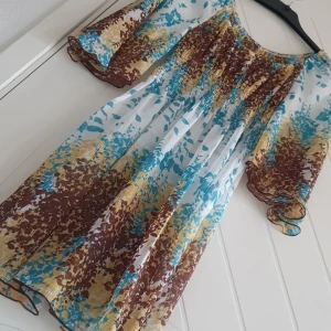 Tunika - Tunika eller kort klänning med flygiga armar, genomskinligt tunnt, blommigt tyg. Lapparna är tyvärr bortklippta. 
