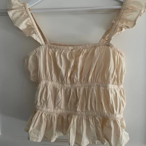 Beige volang-topp - Väldigt fin topp som är cremevit/beige, med volanger och många fina detaljer. Säljer pga att toppen tyvärr inte kommer till så mycket användning. Köptes på zalando, märket River Island. I fint skick!☺️⭐️😊🙏