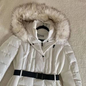 Michael Kors Vinterjacka / Skidjacka - Aldrig använd. Ny med alla prislappar kvar. Har en liten sminkfläck vid halsen efter provning av jackan. Jackan är vit, med svarta detaljer. Klassiska MK-loggan på ärmen är svart. Pälsen är inte riktig, men är lika fluffig och mysig som en äkta. 
