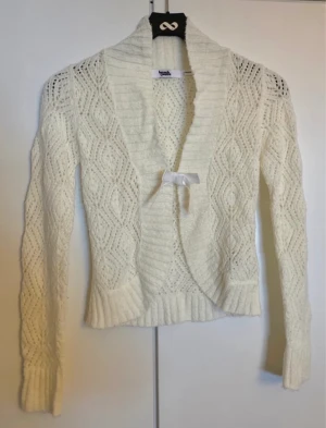 Vit/beige/creme/smutsvit stickad kofta med rosett fina detaljer 146/152/XXS/XS - En vit stickad kofta med rosett fram. Koftan stängs med en hasp. Bra skick, lite nopprig på vissa ställen. Storlek 146/152, kan eventuellt passa XXS/XS också!