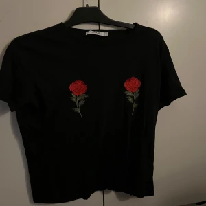 Svart t-shirt - Super snygg t-shirt från NA-KD med två rosor på i st S, använd 1-2 gånger!!!