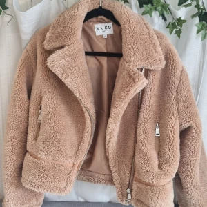 Rosa/beige jacka  - Fluffig jacka från NAKD. Dragkedjor vid armarna och dragkedjor till fickorna 