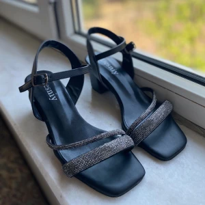 Klackskor med glittrig rem - Eleganta svarta sandaler med fyrkantig tå och glittriga remmar. Sandalerna har en justerbar rem runt ankeln och en bekväm klack, de är helt nya och ör bara använd ett par gånger.