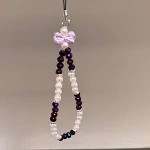 Egentillverkat mobilsmycke med lila o vita pärlor, blingiga mellanplattor och en söt lila. Är totalt 17 cm lång och med en omkrets på ca 18 cm.💜