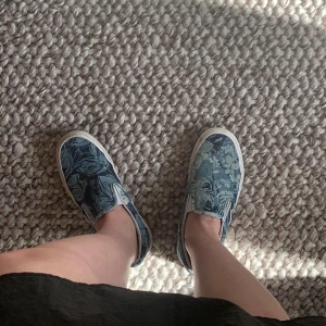 Unika blommiga Vans - Jättefina slip-on Vans i blått jeanstyg! Använda, men fortfarande i mycket fint skick. Kommer tyvärr inte till användning längre. Är storlek 38,5 men passar även mig med 39 🥰