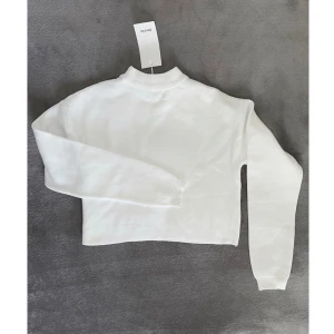 Vit tröja Bershka XS cropped - Färg: vit.  Strl: XS.   Klassisk tröja från Bershka. Jätteskönt och fint material som inte skrynklar. Croppad modell. Perfekt att dra över en klänning en sommarkväll! Eller till ett par slitna jeans! OBS - Helt NY och oanvänd, med lappar kvar!!