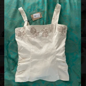 Benvit topp med brodyr - En söt vit topp med fina broderade blommor. Köpt från sellpy med prislappen kvar, jag har aldrig använt den och den är i superfint skick. Har en dragkedja på sidan💗