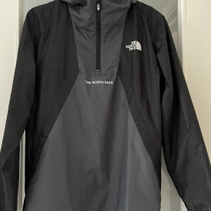 The North Face vindjacka nyskick YXL/XS-S - Vindjacka med huva från The North Face, svart/grå i storlek Youth XL men liknar även XS-S herr/dam. Färgskillnaderna mellan svart och grått inte lika skarpa som på bild. Använd ett par tillfällen förra året innan den blev för liten. 