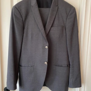 Kostym inkl väst- Tiger of Sweden - Mörkgrå kostym i storlek 46, längd på byxa 101cm. Ord pris 5000kr, reva vid vänster bakficka (se bild 4).