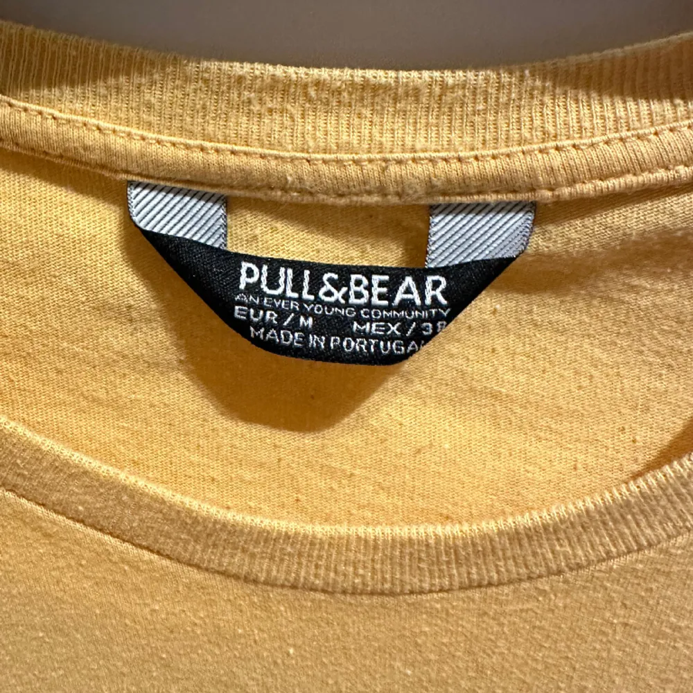 Säljer en mörkgul t-shirt från Pull&Bear med lätt passform. Den är ganska oanvänd och är i bra skick men lite urtvättad. . T-shirts.